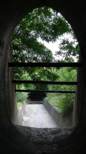 Таким образом, выход тоннеля располагается ниже входа, более чем на метр. Заканчивается тоннель вертикальной стеной более 3м высотой, которая переходит в бетонный каскад с постепенно снижающимися уступами.